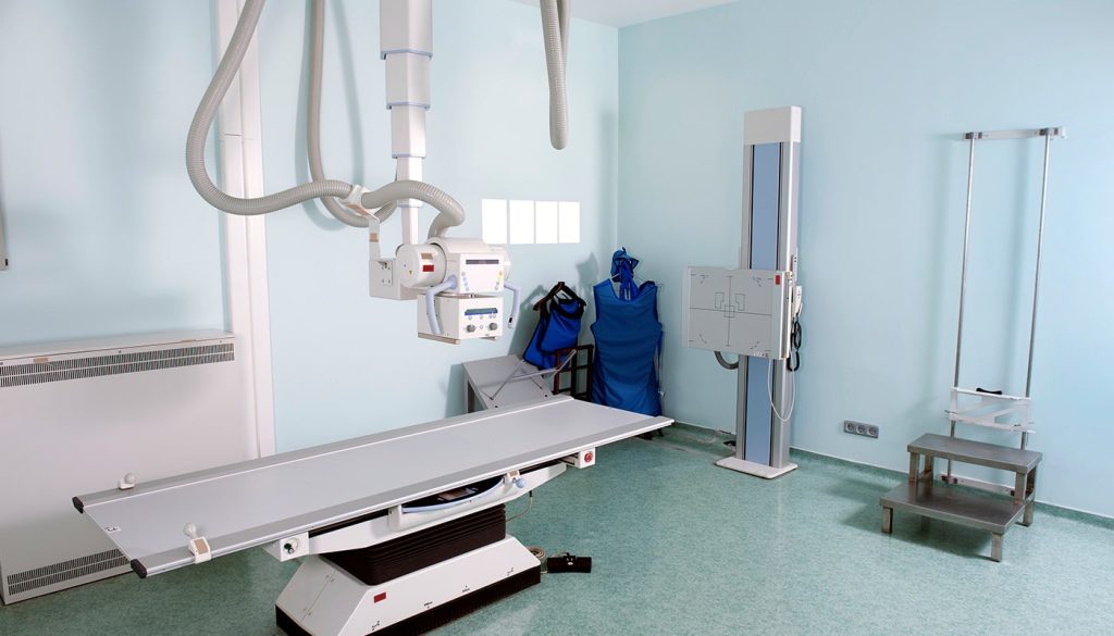 Maintaining X-ray machine parts is important for the wellness of your X-ray machine. The image shows an X-ray machine in a room with pastel blue walls.