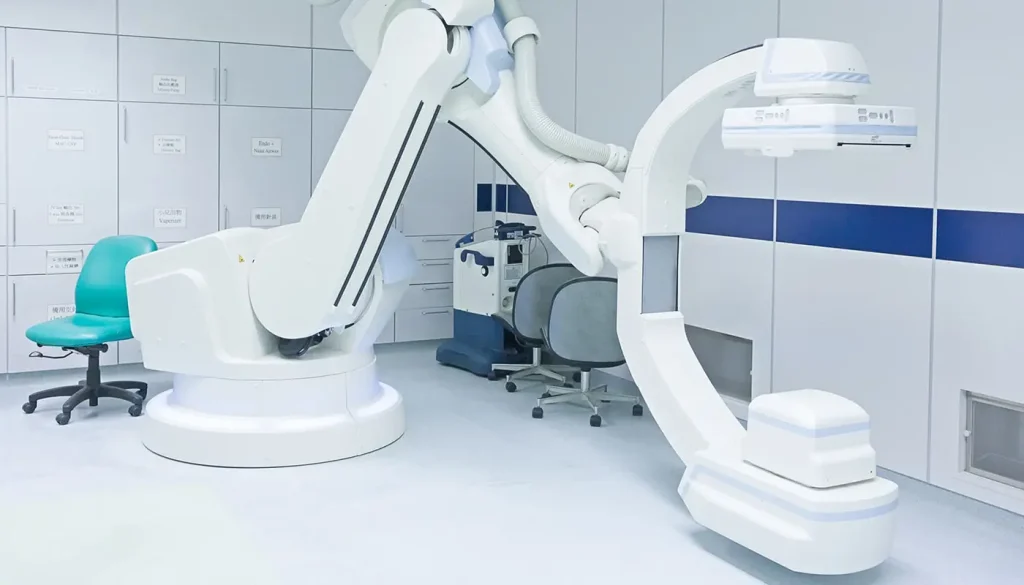 A c-arm x-ray machine kept in a room with chairs on the side. The room has white walls with a big blue horizontal stripe.