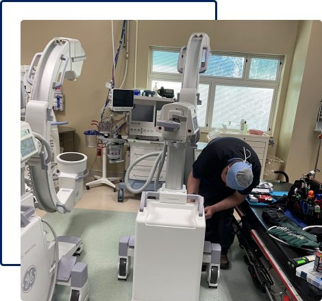 An expert technician repairing a C-arm machine in a room full of other medical imaging instruments.